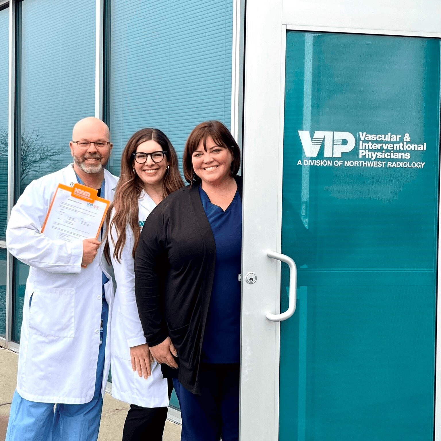 Drs. Flanders and Frankum and a member of the office staff posing for a photo in front of the VIP logo on the door